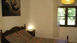 Una cama bien tendida con una colcha estampada, una lámpara de noche y una ventana con cortinas.