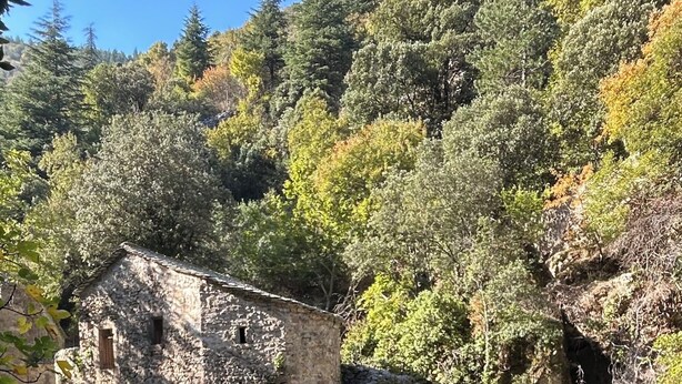 Un bâtiment en pierre doté d’une entrée en forme de tunnel, entouré d’une végétation luxuriante et d’une cascade.