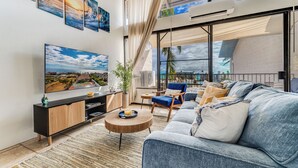 Una sala de estar moderna con un televisor grande, asientos cómodos y vista al océano.