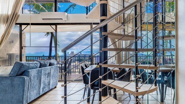 Un interior moderno con una escalera, zona de estar y grandes ventanales que ofrecen vistas de la ciudad.