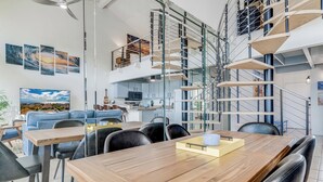 Un interior moderno con una mesa de comedor de madera, sillas de cuero negro, un sofá azul y una cocina al fondo.