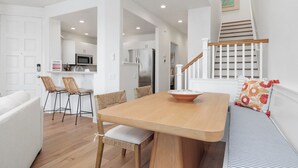 Une cuisine moderne avec des meubles blancs, une table à manger en bois et un escalier doté d’une rampe blanche.