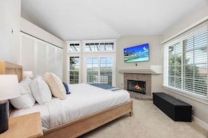 A bedroom with a bed, a fireplace, a TV, and large windows.