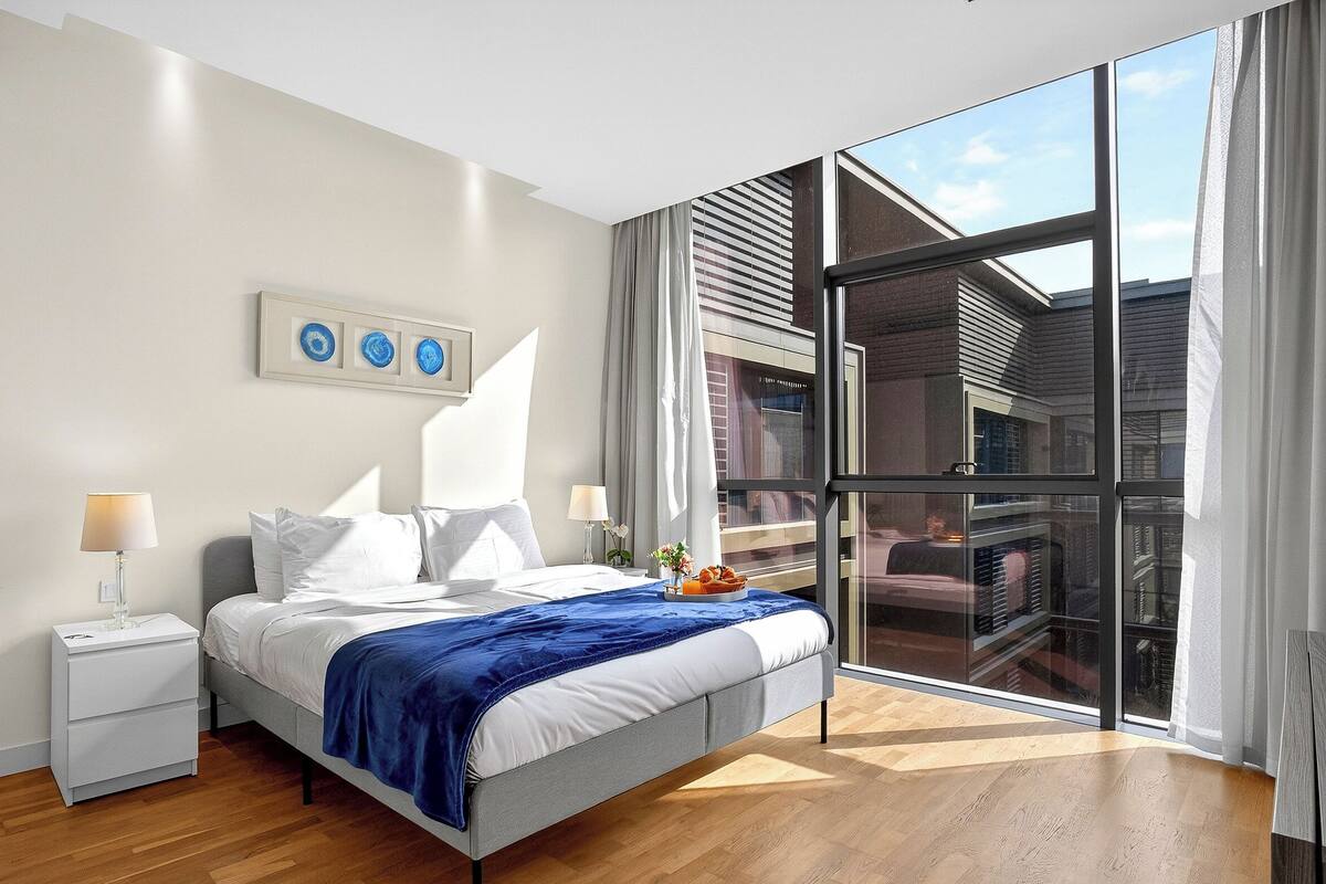A modern bedroom with a bed, bedside tables, a large window, and a view of the outside.