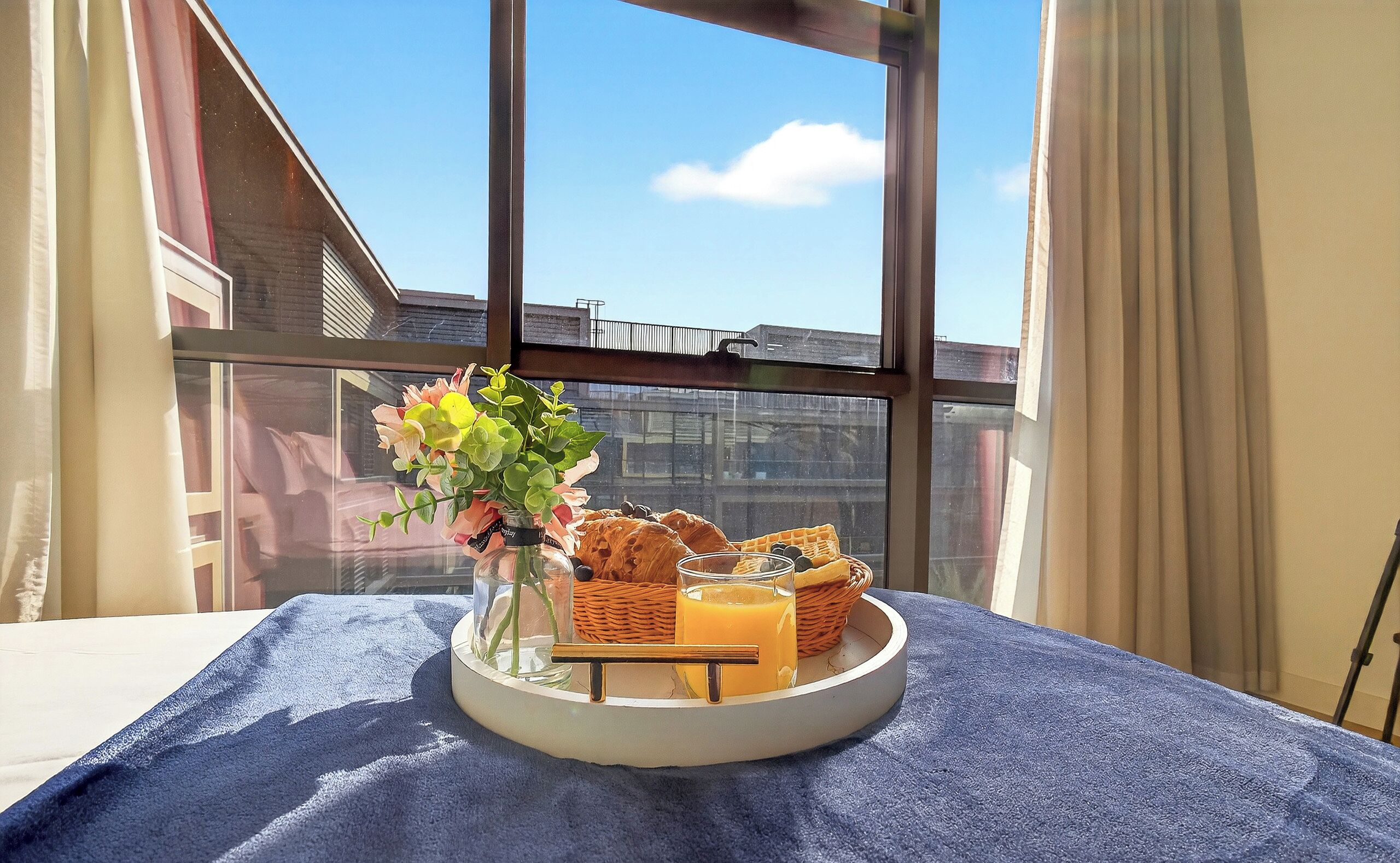 A breakfast tray with pastries, a glass of orange juice, and a vase of flowers on a table by a window.