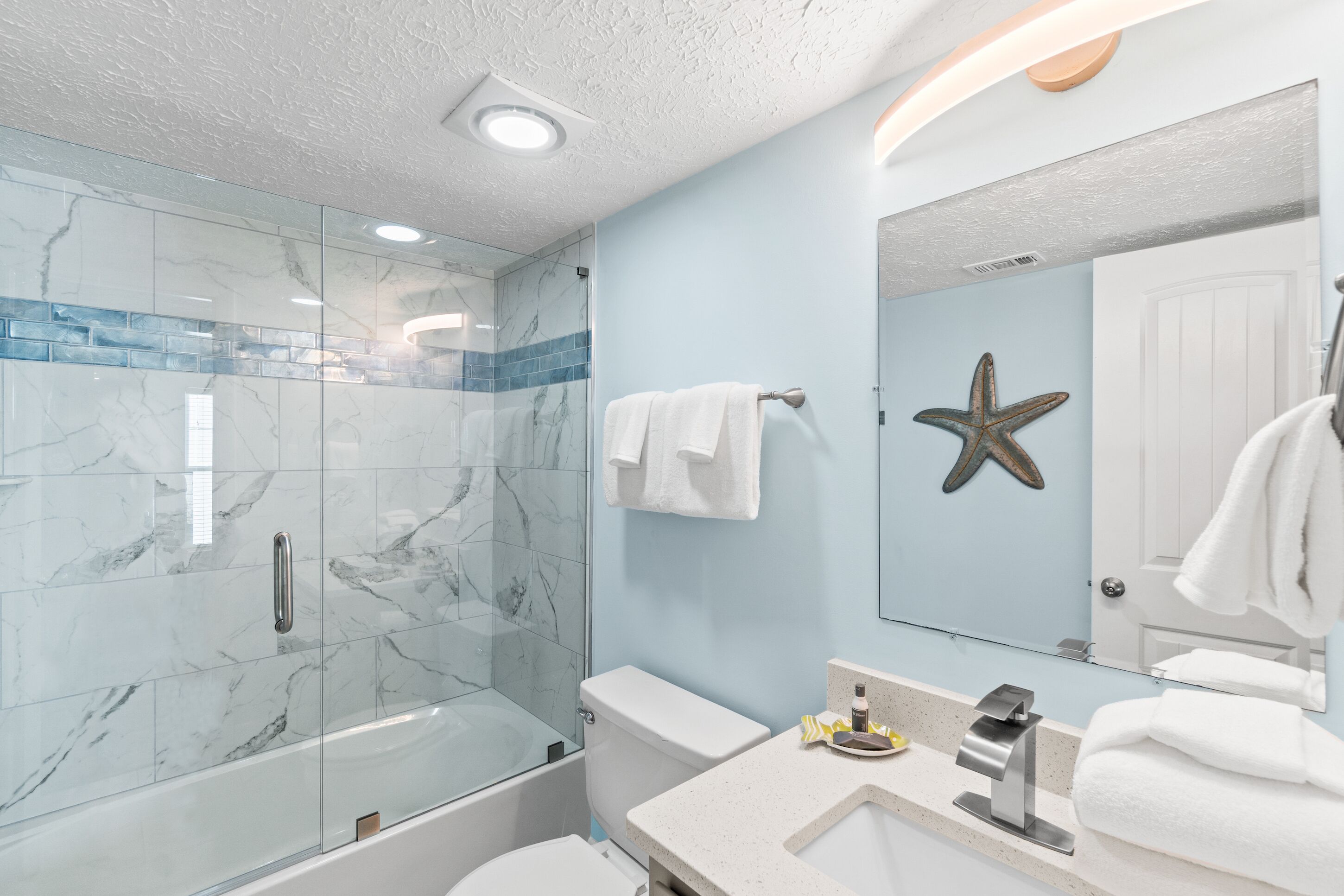 A modern bathroom with a glass-enclosed shower, a white toilet, a sink with a mirror, and a starfish decoration on the wall.