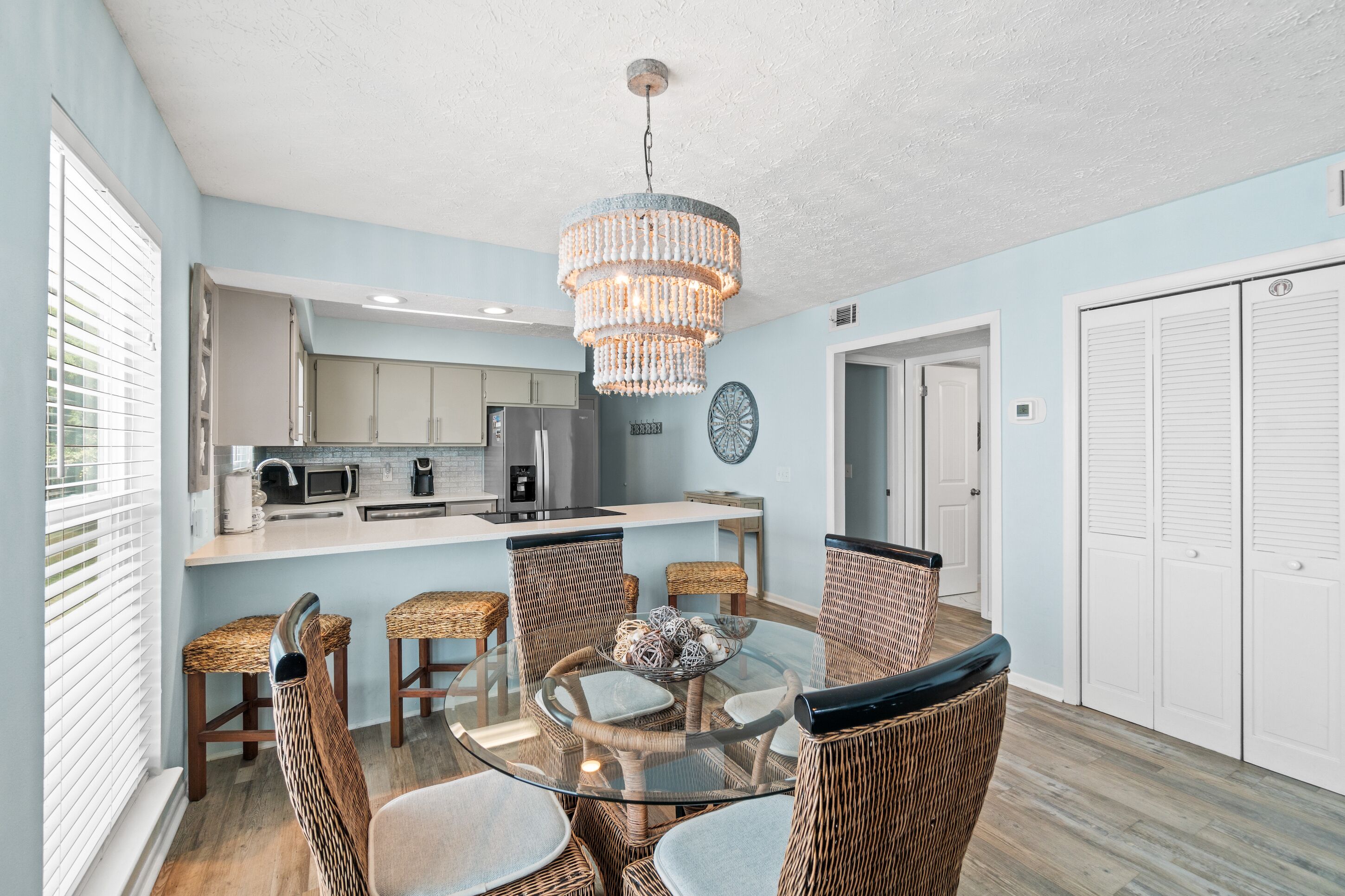 A dining area with wicker chairs, a glass table, and a chandelier.