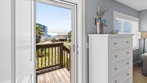 Ein Zimmer mit Holzterrasse, weißem Schminktisch und Blick auf ein blaues Gebäude und einen Strand.
