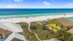 Blick auf einen Strand mit blauem Himmel, feinem Sand und einem gelben Gebäude mit Balkon.