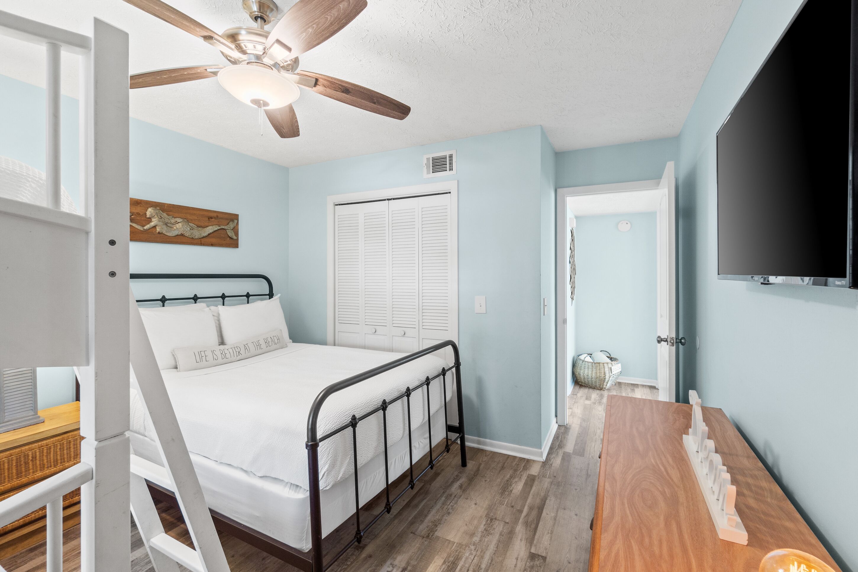 A bedroom with a bed, a ceiling fan, a window with shutters, a television, and a wooden dresser.