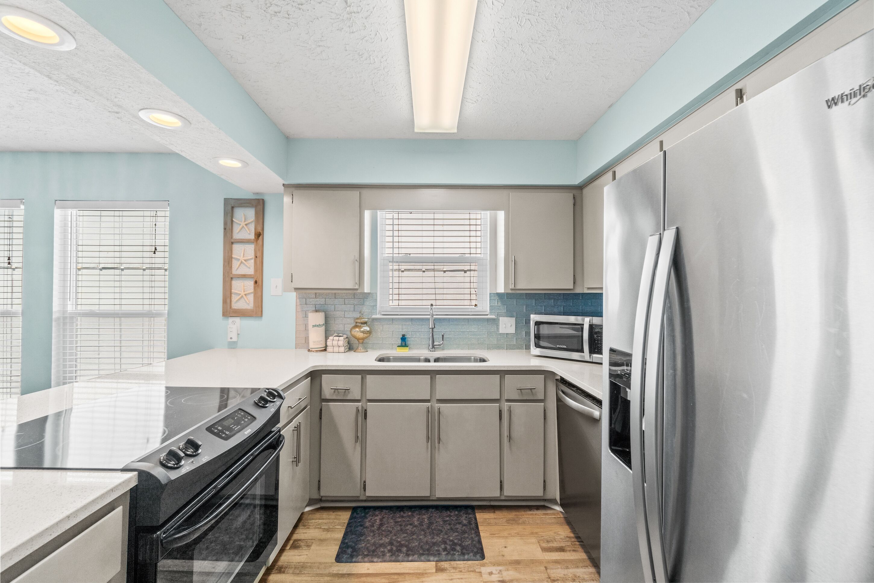 A modern kitchen with grey cabinets, a stainless steel refrigerator, a microwave, and a stove.