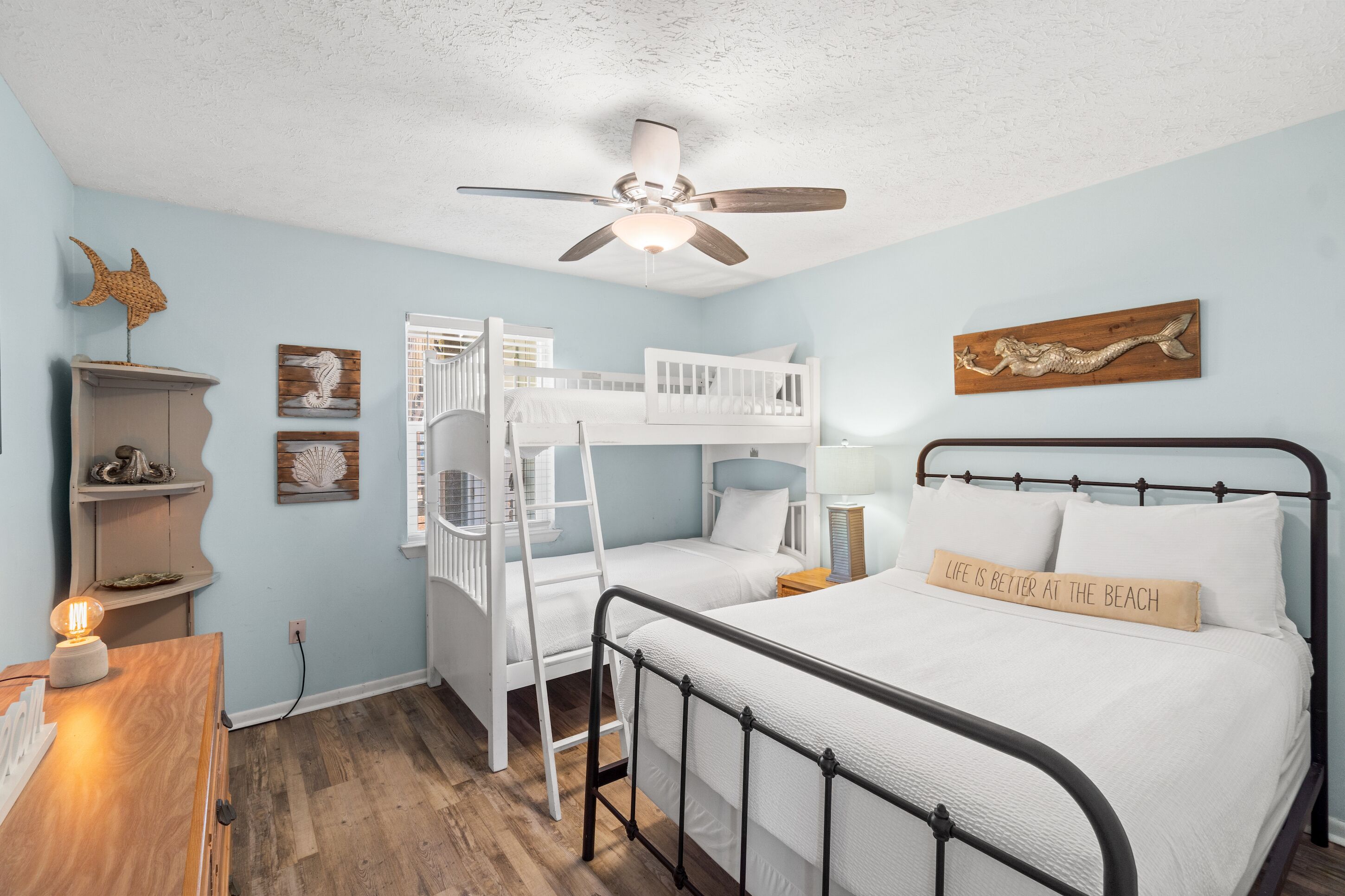 A bedroom with a bunk bed, a single bed, a ceiling fan, and a wall-mounted shelf.