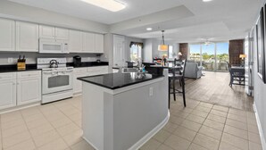 A modern kitchen with white cabinets, a central island, and a dining area with a view. - Yacht Club Villas #2-401 Relaxing Waterway View in Barefoot Resort! (North Myrtle Beach)
