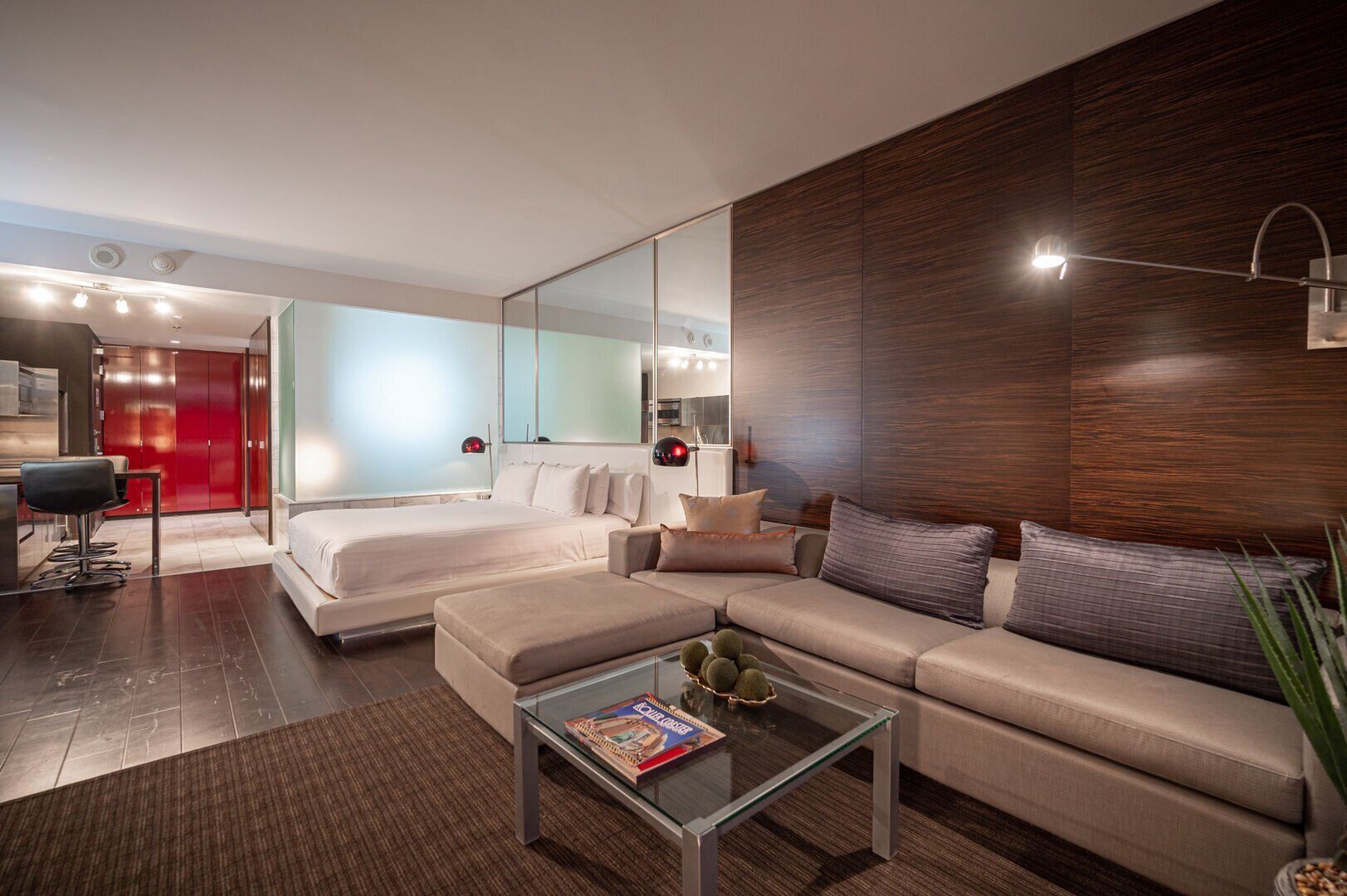 Een moderne hotelkamer met een bed, een bank, een glazen salontafel en een grote spiegel.