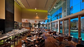 Um restaurante amplo com mesas comunitárias alongadas, área de bar e grandes janelas com vista para o exterior.