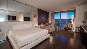 Quarto de hotel moderno com uma cama grande, um sofá, uma escrivaninha e uma varanda com vista para a cidade.