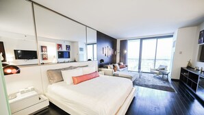 Una habitación de hotel moderna con una cama grande, televisor, sofá y balcón con vistas.