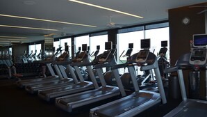 Un gimnasio con varias cintas de correr y bicicletas estáticas, ventanas amplias y un ventilador de techo.