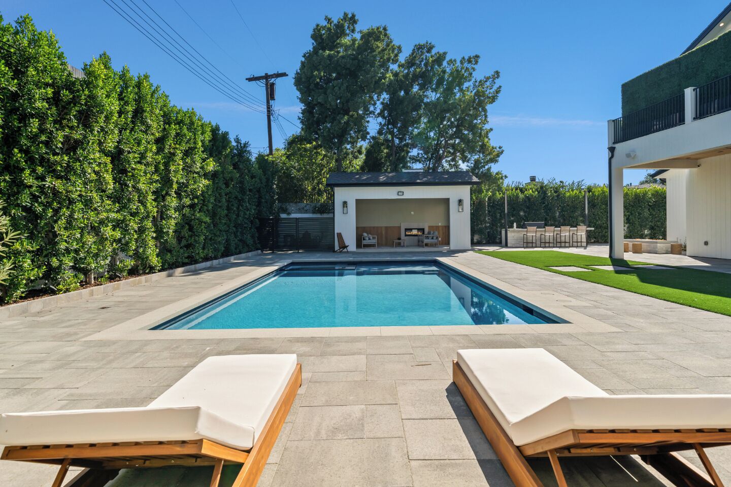 A rectangular swimming pool with two lounge chairs in the foreground, surrounded by a paved patio.