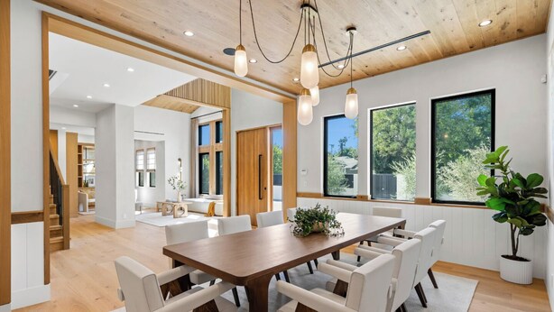 A spacious dining area with a wooden table and white chairs, large windows with a view of greenery, and a modern ceiling design. - Genesta Villa - A Contemporary Modern Villa w/ Pool, Spa & Theater (Encino)