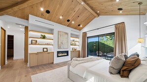 A modern bedroom with a large bed, a fireplace, a view of greenery, and a wooden ceiling. - Genesta Villa - A Contemporary Modern Villa w/ Pool, Spa & Theater (Encino)