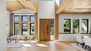 A spacious living area with a wooden ceiling, large windows, a sofa, and a dining table. - Genesta Villa - A Contemporary Modern Villa w/ Pool, Spa & Theater (Encino)