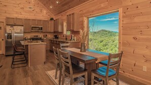 Een houten keukentje met een groot eiland, houten keukenkastjes en uitzicht op een bebost landschap.