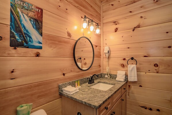 A wooden cabin bathroom with a granite sink, a mirror, a hairdryer, and a poster of a waterfall.