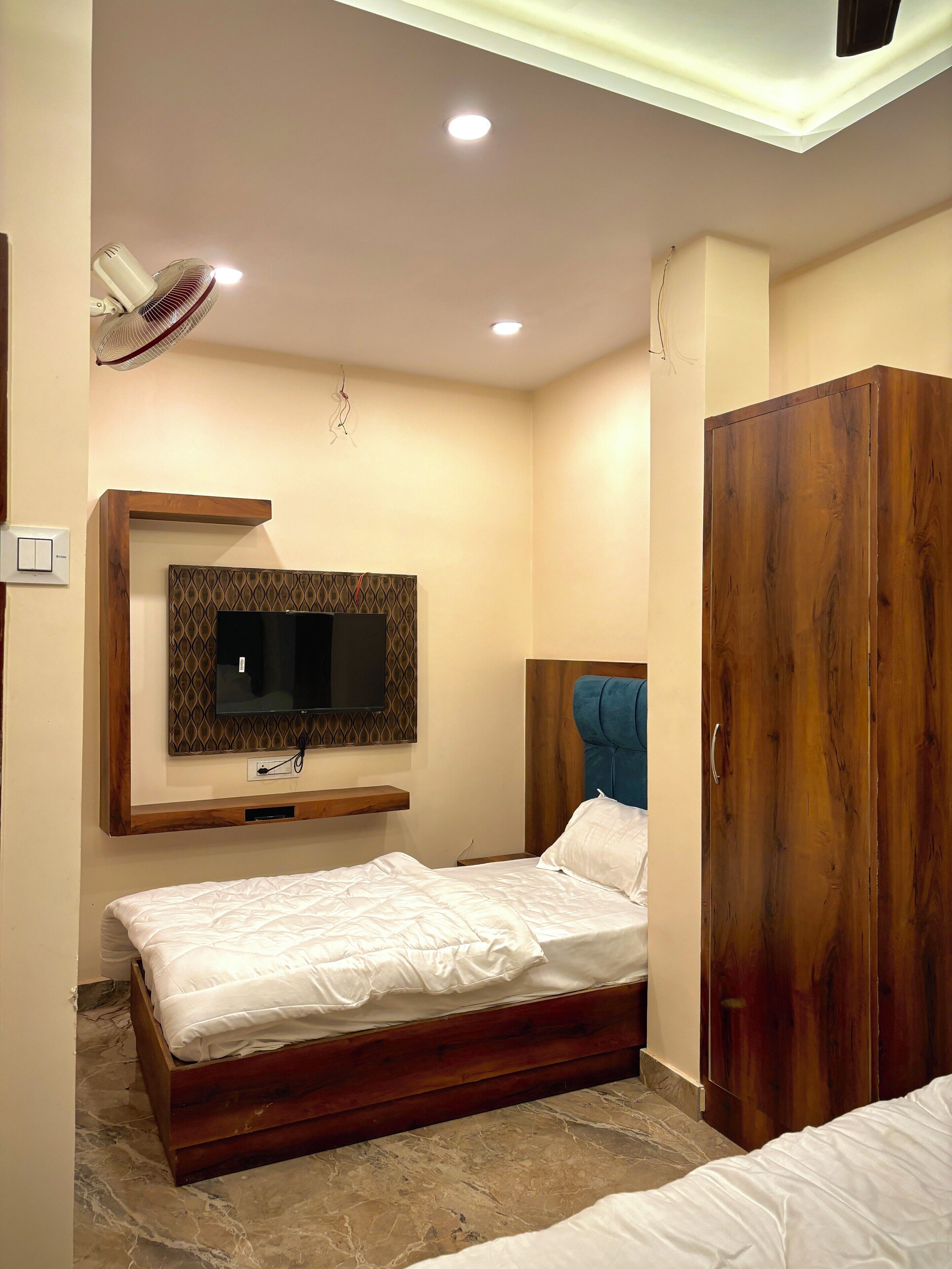 A bedroom with a bed, a wooden wardrobe, a mounted TV, and a ceiling fan.