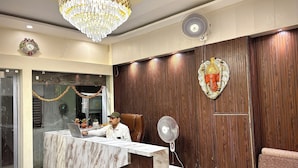 A reception area with a marble counter, wooden paneling, a chandelier, and a wall-mounted fan. - VIA GANGA INN Varanasi (Varanasi)