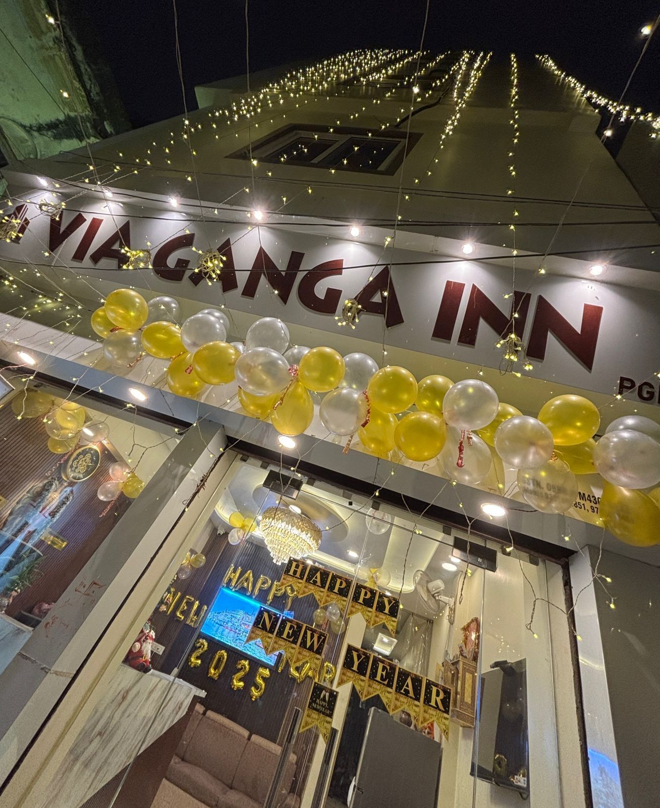 A hotel entrance with a 'Happy New Year' sign, balloons, and string lights.