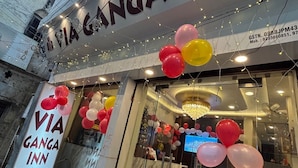 The exterior of a hotel named VIA GANGA INN with a signboard, balloons, and a reception area visible through the glass doors. - VIA GANGA INN Varanasi (Varanasi)