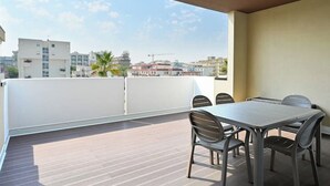 A balcony with a table and chairs, overlooking a cityscape with buildings and palm trees.