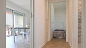 A hallway with a glass table and chairs, a bed with a patterned bedspread, and a tiled floor.