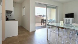 A modern kitchen with a built-in stove, a dining area with clear chairs and a glass table, and a balcony with a view of the city.