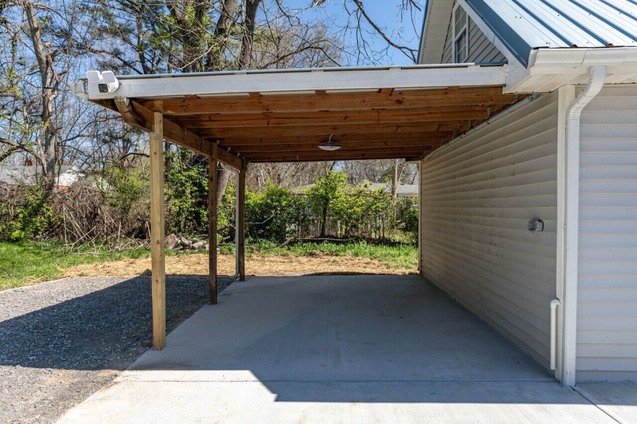 A covered garage with a concrete floor, wooden beams, and a metal roof.