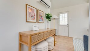 Un couloir propre et moderne, avec une console en bois, deux tableaux abstraits encadrés, une plante en pot et une porte équipée de stores.