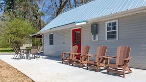 Une petite maison avec une porte rouge, un porche abrité et quatre chaises Adirondack en bois.