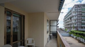 A balcony with a view of a building under construction. There are two white plastic chairs and a small table.