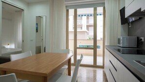 A compact kitchen with a microwave, a dining table with chairs, and a sliding glass door leading to a balcony.