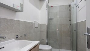 A modern bathroom with a glass-enclosed shower, a white bathtub, and a toilet.
