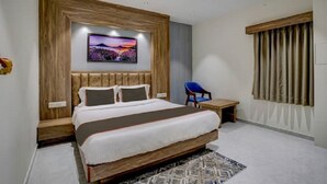 A bedroom with a large bed, a small table, a chair, a ceiling fan, and a window with curtains. - Hotel SR Inn (Anand)