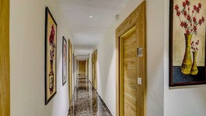 A hotel hallway with framed artwork on the walls, wooden doors, and a marble floor. - Hotel SR Inn (Anand)