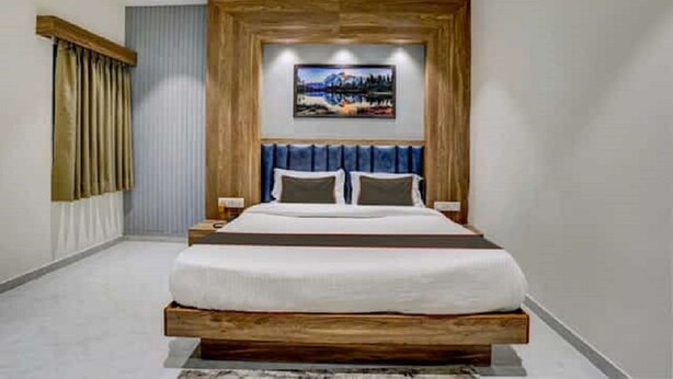A modern bedroom with a wooden headboard, a large bed, and a painting above it. - Hotel SR Inn (Anand)