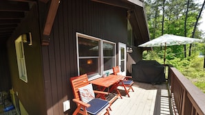 Une terrasse en bois avec une table et des chaises, un barbecue abrité et une vue sur la forêt environnante.