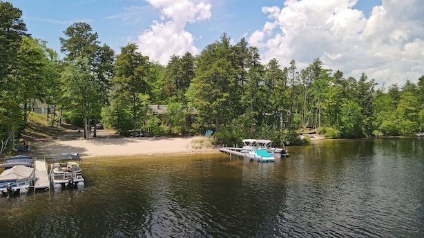 Une propriété au bord du lac, dotée d’un quai, de bateaux et d’une plage de sable entourée d’arbres.