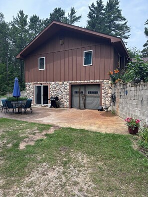 Une maison à deux étages avec des fondations en pierre, un garage et un patio aménagé avec du mobilier d’extérieur.