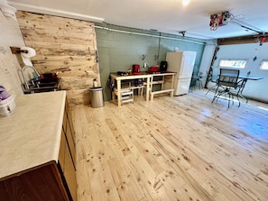 A compact kitchen with a wooden floor, a sink, a table with chairs, and a refrigerator. - Whitefish Walkout-walk to Lake Superior Beach! (Paradise)