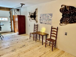 Ein Zimmer mit Holzboden, zwei Holzstühle, einem kleinen Tisch, einer Karte an der Wand und einem Fellteppich.