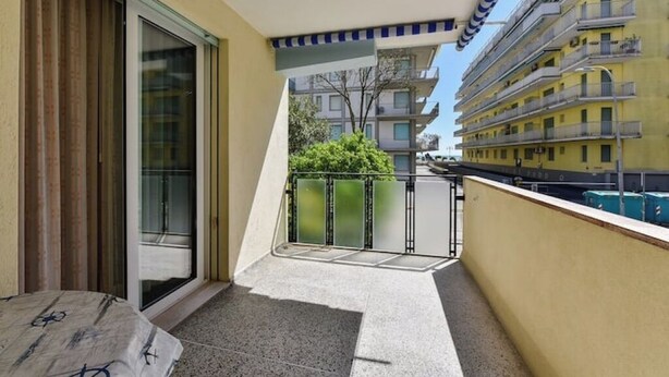 A balcony with a glass door, a small rug, and a metal railing.